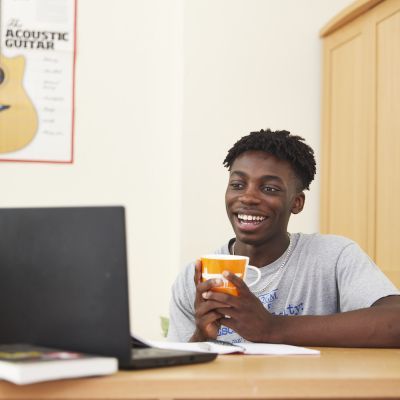 A boy holding a mug and sitting at a laptop